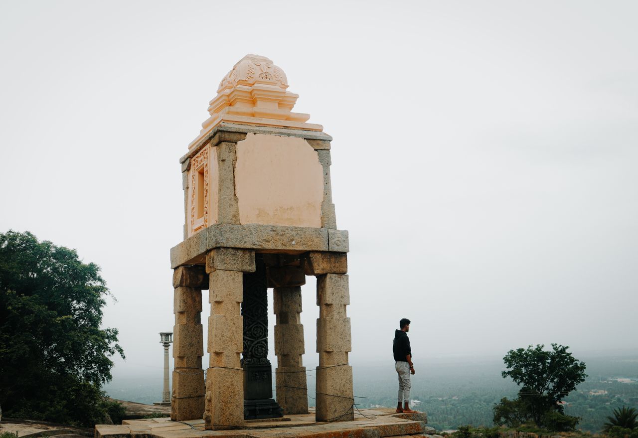 A man stands beside a historic stone pavilion on a foggy day, evoking a sense of solitude.